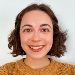 Britt, a white woman with short curly brown hair, is seen from the shoulders up. She is smiling.